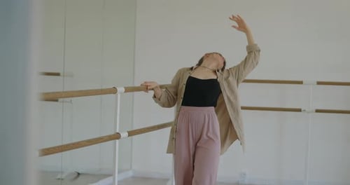 Young Girl Stretching and Reaching Back While Holding Onto Ballet Bar and Performing Classical