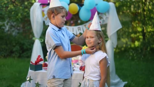 Irmão vestindo chapéu de festa para a irmã mais nova rindo enquanto a câmera ao vivo amplia o retrato com vista lateral