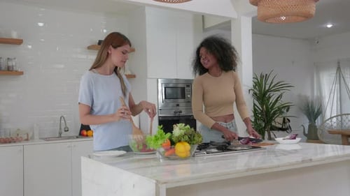 Young Women Preparing Salad Together in Bright Kitchen