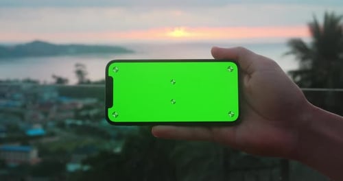 Close Up Holding Smartphone Horizontal Position with Green Screen Chroma Key Over Sunset at Sea at