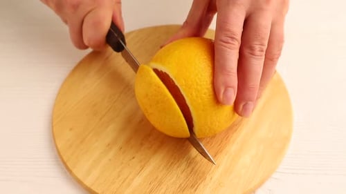 Male hand cuts fresh orange with a knife on wooden kitchen board