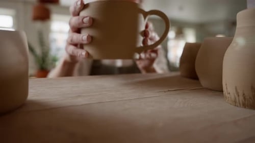 Closeup of Handcrafted Ceramics with Artisan Blurring Coffee Mug in Pottery Workshop