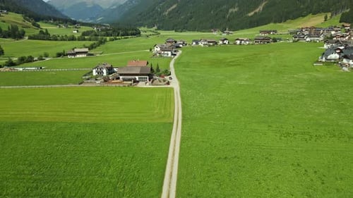 An alpine village is nestled among lush green fields and surrounded by forested mountains. Tradition