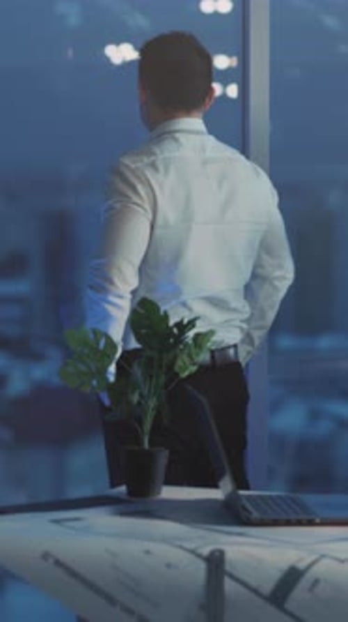 Man Contemplating City View from Office at Night