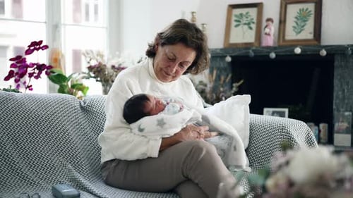 Senior Woman Holding Newborn Baby on Couch Indoors