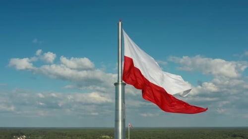 The flag of Poland flutters in the wind against the panorama of the country.