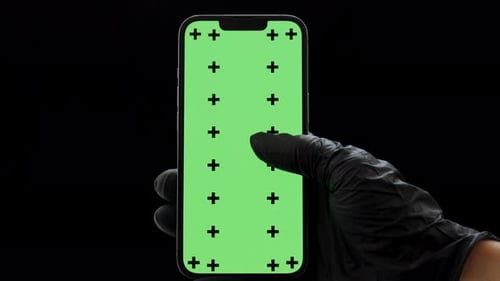 Une main dans un gant en nitrile noir tenant un smartphone et faisant défiler un écran vert avec