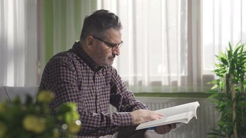 Man Sitting on Couch Reading Book Indoors