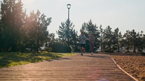 Healthy Young Active Couple in Sportswear Jogging along Wooden Road