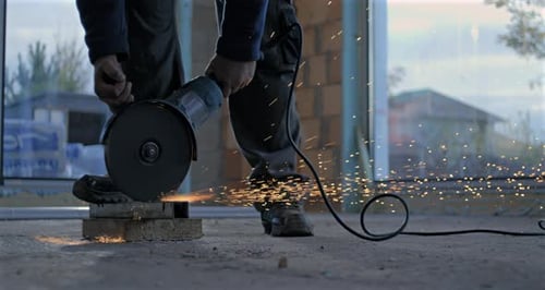 Using angle grinder indoors with sparks flying, grinding on concrete floor, industrial construction