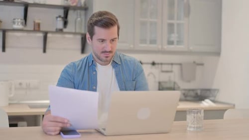 Worried Man Looking at Documents and Laptop Indoors