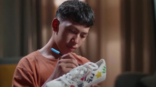 Close Up Of Asian Boy Footwear Designer With A Desktop Computer Putting Coloured On Sneakers At Home