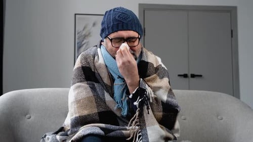 Man Sick with Cold wrapped in Blanket Indoors