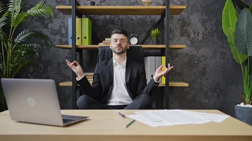Bearded Businessman Sits in Lotus Position Resting in Office