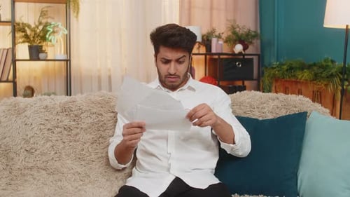 Man Reading Document Looking Frustrated on Couch Indoors