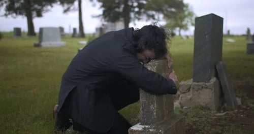 Emotionaler, depressiver Mann trauert auf dem Friedhof um das Grab einer verlorenen Familie.