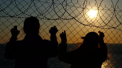 Refugees Looking at Sunset Behind Barbed Wire Fence