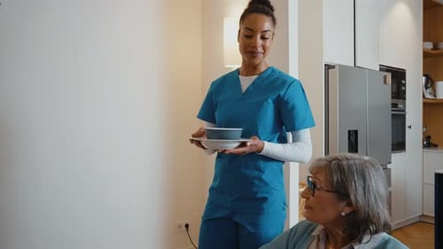 Friendly caregiver delivers meal to senior woman at home