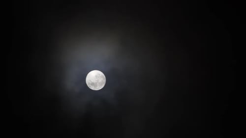 Clouds pass in front of Full Moon in a dark sky