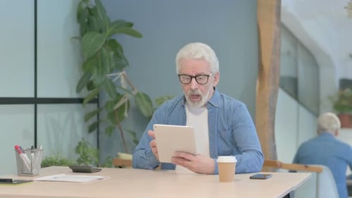 Senior Man Uses Tablet at Table Indoors