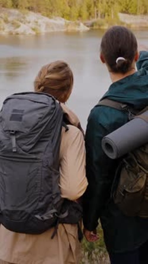 Couple with Backpacks Admiring Lake Among Autumn Forest