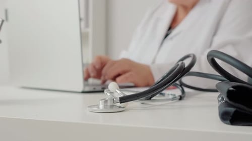 Stethoscope with doctor reading research report background on laptop in hospital.