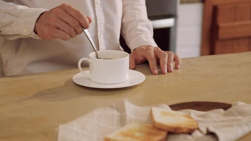 Man Stirs Coffee at Home in Morning Light