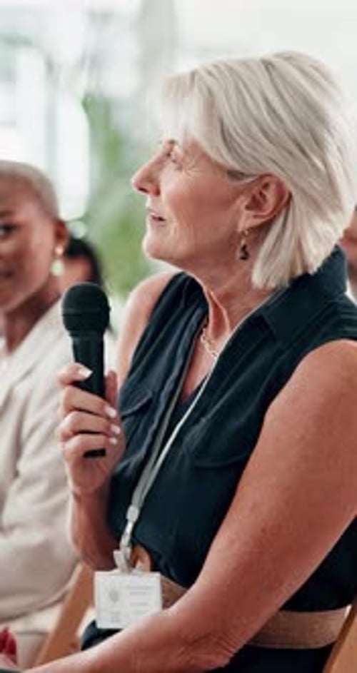 Senior woman, microphone and audience at conference for smile, question and agenda for info