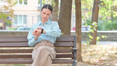 Woman Using Smart Watch on Park Bench