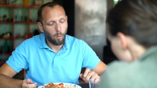Man Eating Spaghetti with Friend Inside Modern Restaurant
