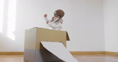 Ein als Flieger oder Pilot verkleidetes Mädchen im Schlafzimmer tut so, als würde es ein Papierflugzeug fahren und stellt sich vor