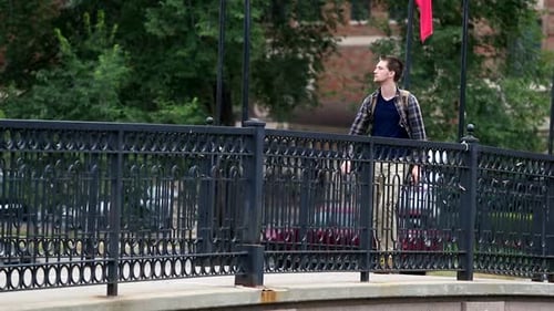 Stunning young man walks across bridge with his backpack on.