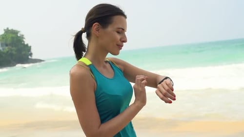 Woman on tropical beach checks pulse on smartwatch during summer vacation