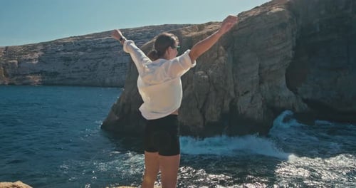 Slow Motion of Woman Raising Her Arms Uphill on the Edge of Cliff Near the Ocean