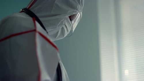 Unrecognized doctor in protective suit holds tablet checking patient history hospital ward