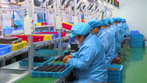 Arbeiterinnen in einer Elektronikfabrik, die gedruckte Leiterplatte in blauem Arbeitsmantel zum Schutz der Montage herstellen