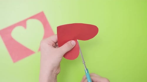 Cutting Red Paper for Valentine Card on Green Background