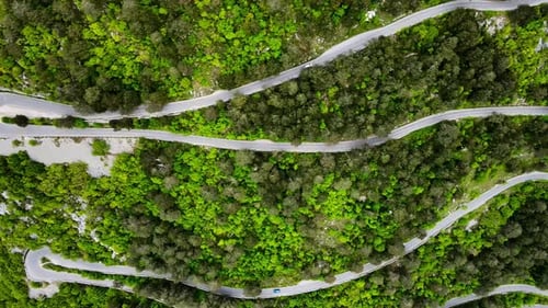 Aerial top down view of mountain serpentine road with moving cars. Road uphill with many sharp turns