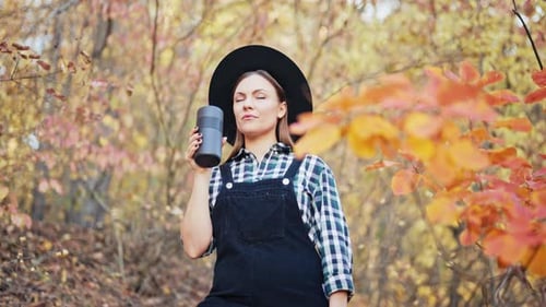 Hipster Woman Drinking Hot Coffee or Tea Thermos Golden Park Forest in Autumn