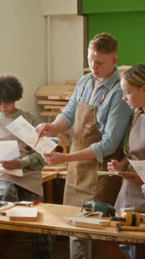 Vertical of Carpenter Explaining How to Read Woodworking Plan to Teenagers