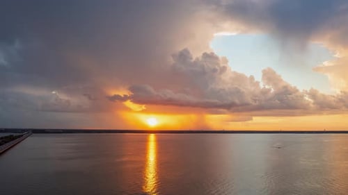 Sun sets and reflections golden yellow ray across lake, storm clouds billowing and growing
