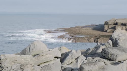 Rocky cliff in the foreground, waves crashing and splashing in slow motion in the background. Oceani