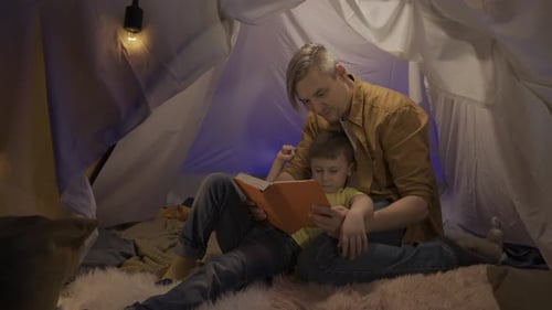 Man and Child Read in Blanket Fort at Night