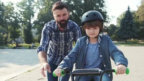 Father and Son Learning to Ride in Big Park of City Dad Looking Son Riding Away Leisure Family