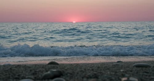 Fundo romântico do pôr do sol no mar. Horizonte roxo e ondas rolavam em direção a uma praia de calhau
.