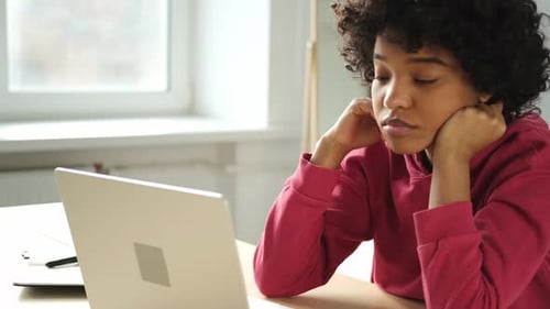 African American Woman Sitting at Table Stretching Massaging Neck Taking Break From Work on Laptop