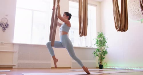Athletic Woman Practicing Aerial Yoga in Bright Studio