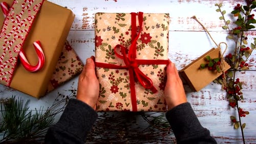 Top view of hands removing gifts one by one from a festive arrangement. Holiday-themed scene with wr