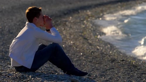 sad pensive guy with sitting by the sea reflecting in loneliness