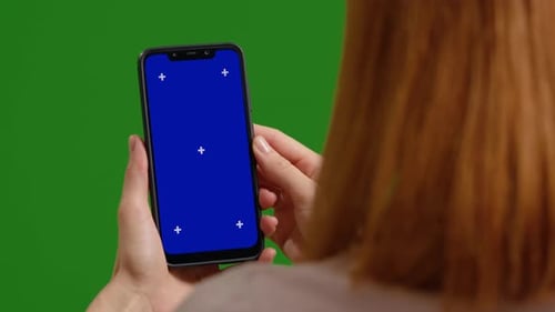 Woman taps blue phone chroma key while on green screen studio.